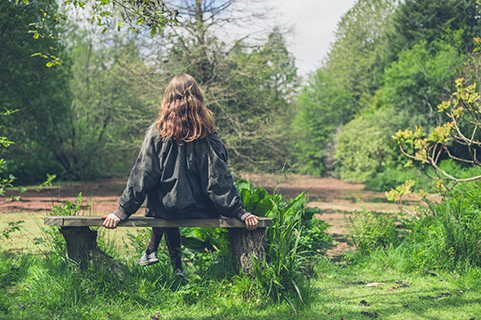 A woman sitting on a bench by a lakeside path in contemplative thought.